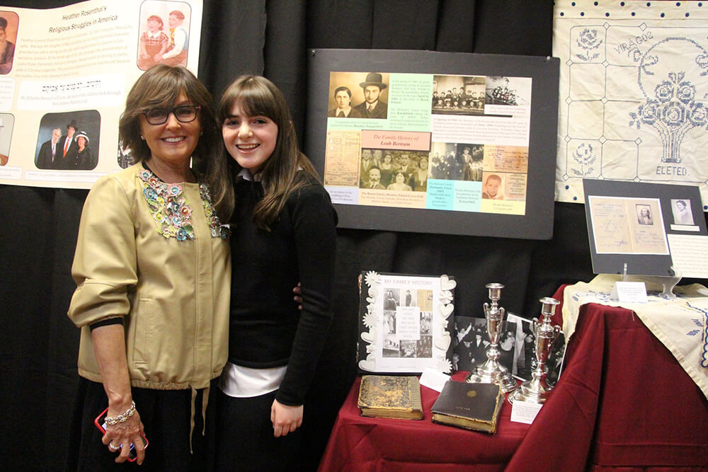 Chani Gotlieb, left, with female student standing in front of exhibit at the Genealogy Project